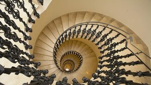 Un escalier en colimaçon avec un mur de couleur beige et des balustres noires.