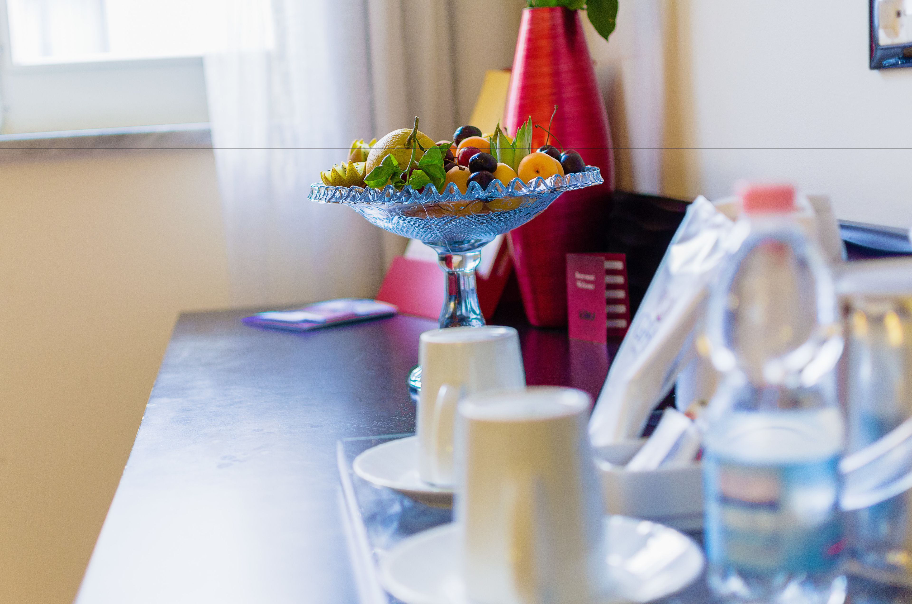 A dining table with a fruit bowl, cups, and a water bottle.
