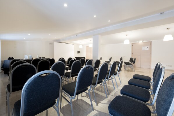 Une salle de conférence avec des rangées de chaises, un pupitre et une porte au fond.