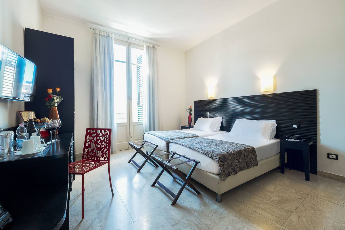 Une chambre d’hôtel moderne, équipée d’un lit, de tables de chevet, d’un bureau avec une chaise, d’une télévision et d’une fenêtre avec des rideaux.