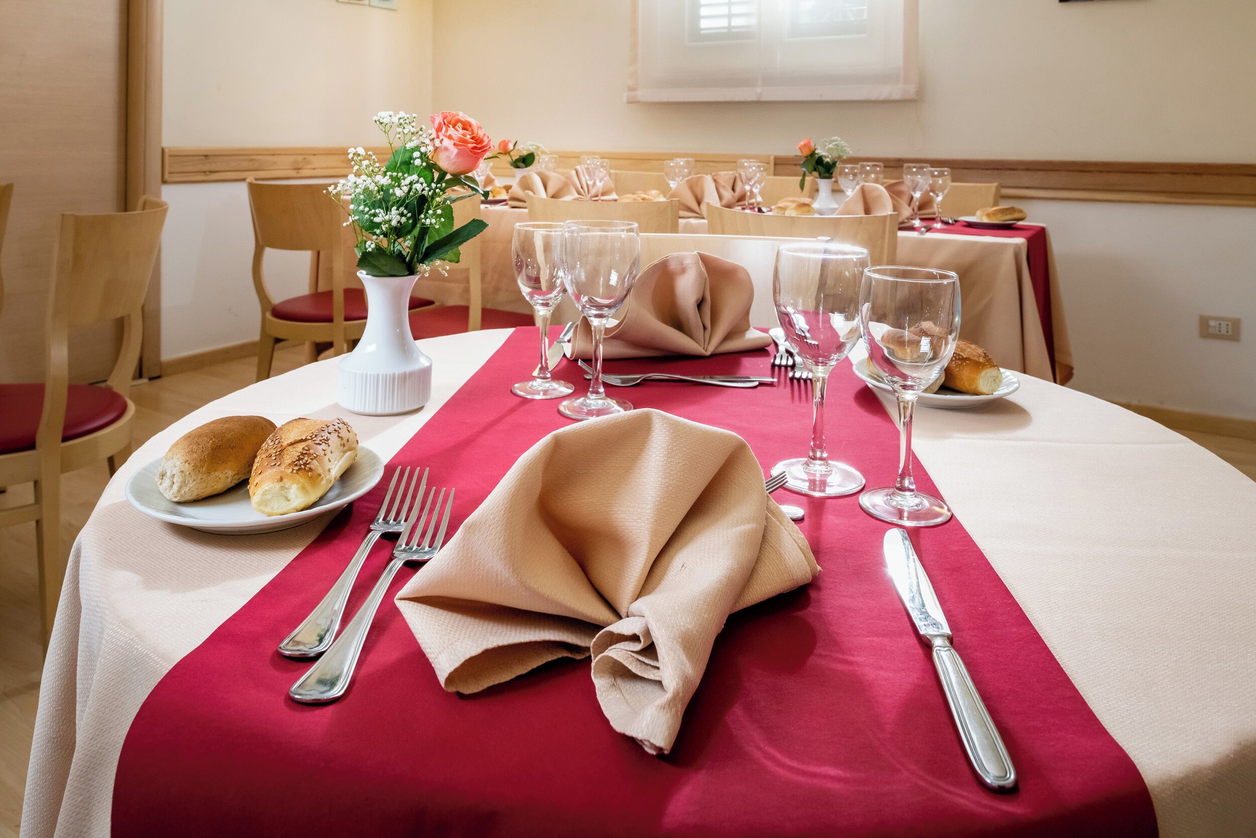 Una mesa de comedor con mantel rojo, cubiertos y servilleta doblada.