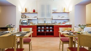 Une cuisine moderne avec des meubles de rangement rouges, des tables et des chaises en bois. On y trouve plusieurs étagères remplies d’ustensiles de cuisine et un îlot central doté d’un évier.