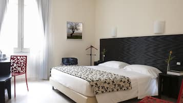 Una camera d'albergo con un letto, una scrivania, una sedia, un comodino e un quadro appeso al muro.