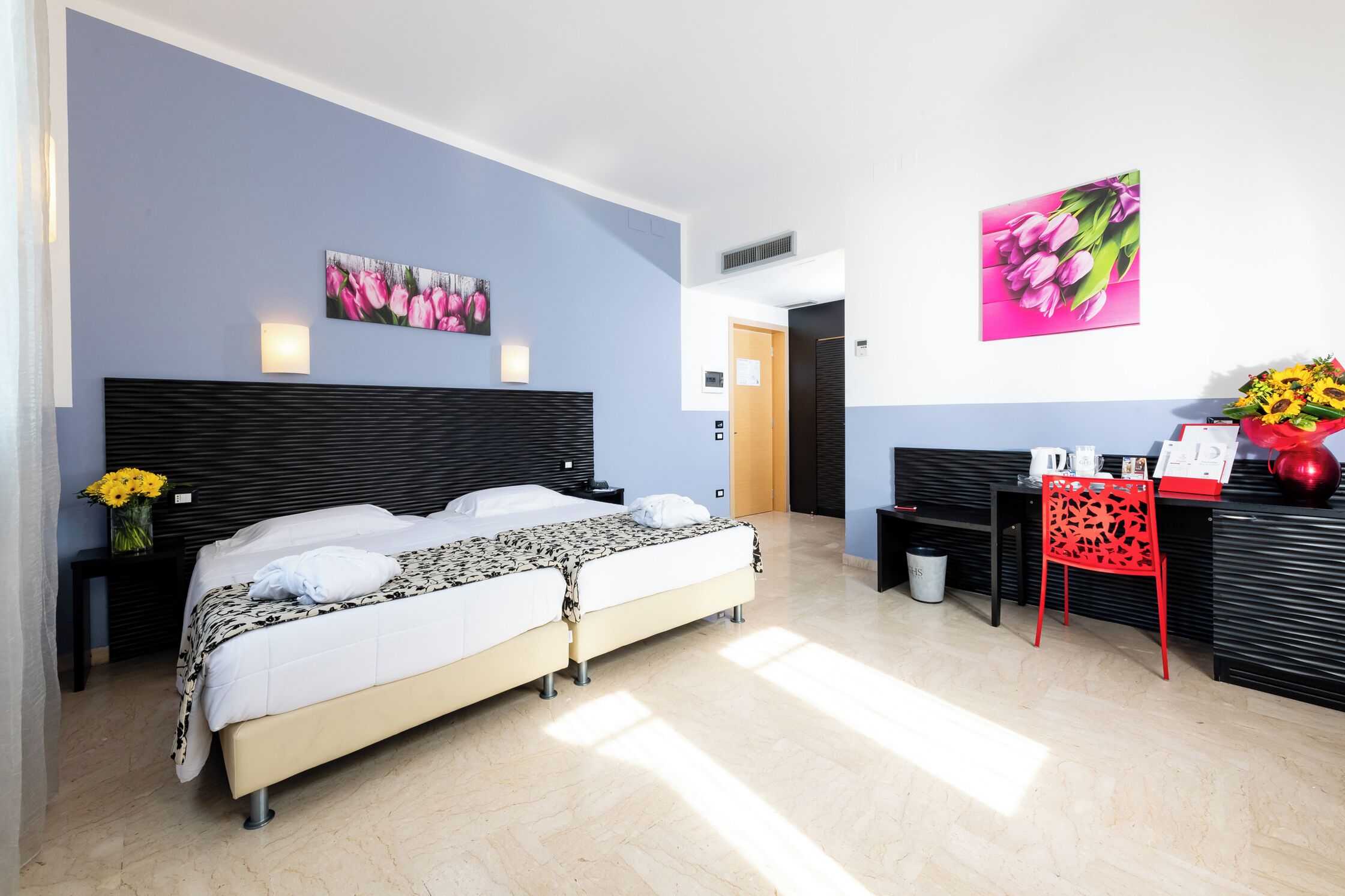A modern hotel room with a large bed, a desk, and two wall-mounted lamps.