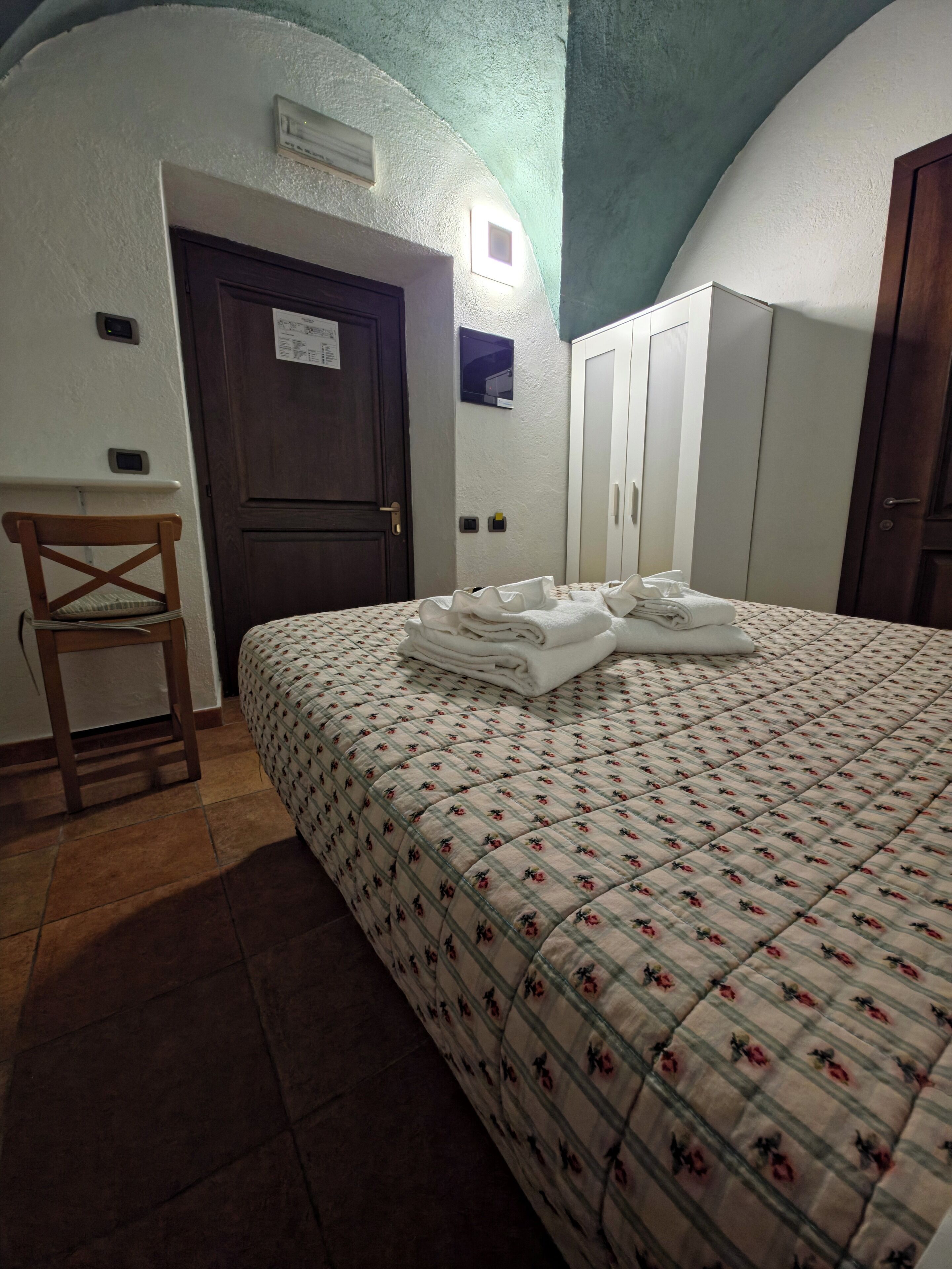 Ein Schlafzimmer mit einem Bett, einem Holzstuhl, einem Kleiderschrank und einer Tür.