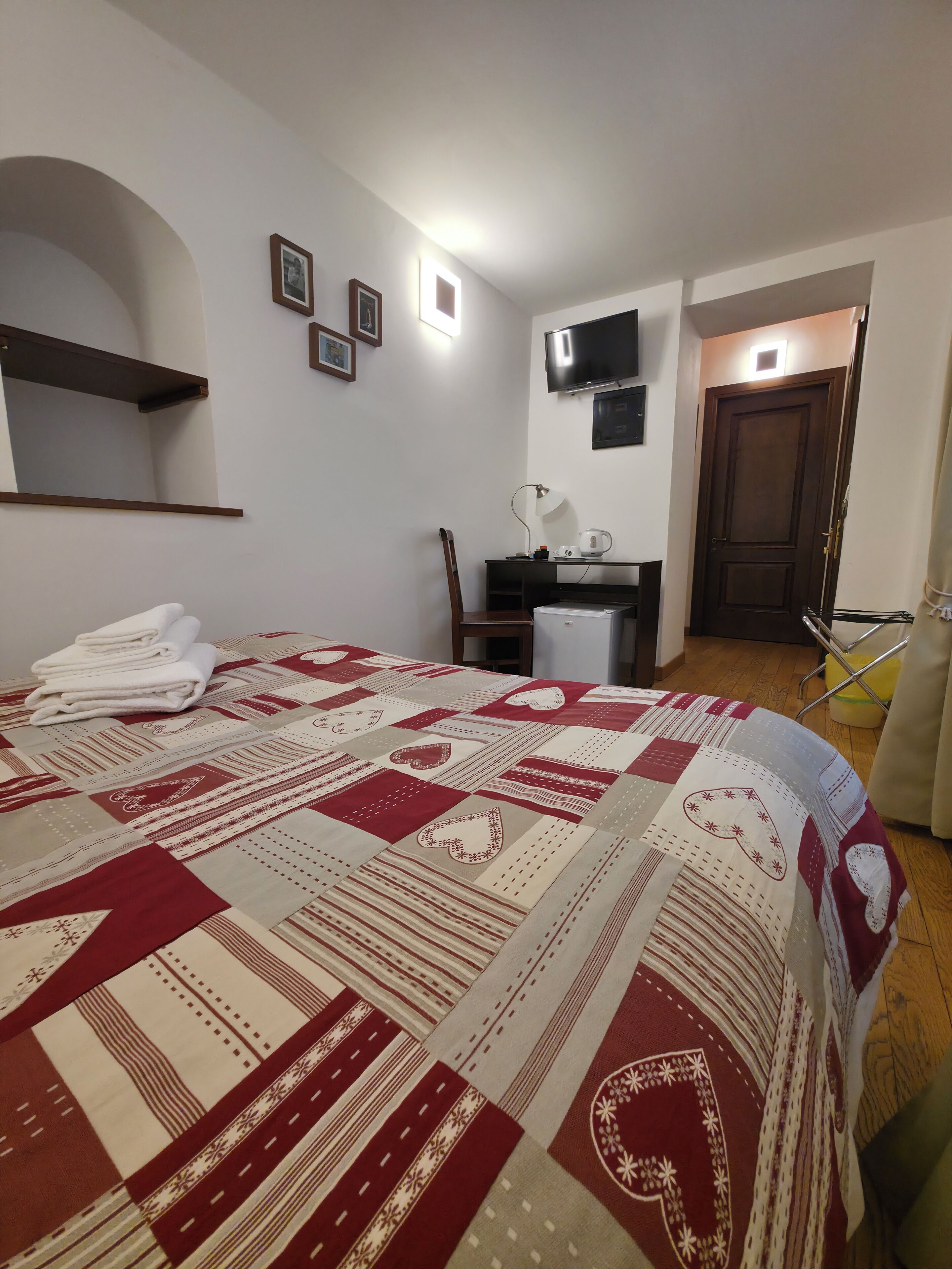 Una camera d'albergo con un letto, una scrivania, una sedia, un televisore e una porta.