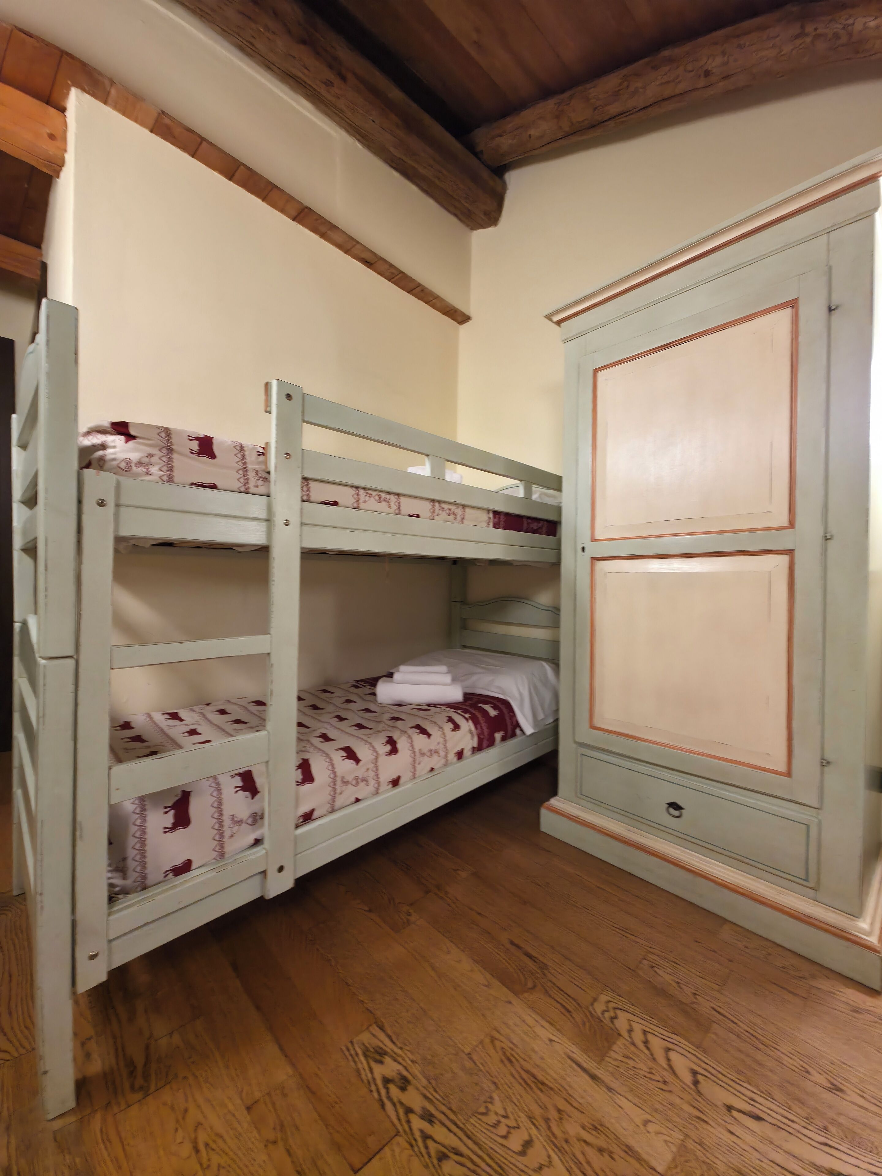 Een stapelbed met beddengoed met een patroon, een houten garderobe en een houten vloer.