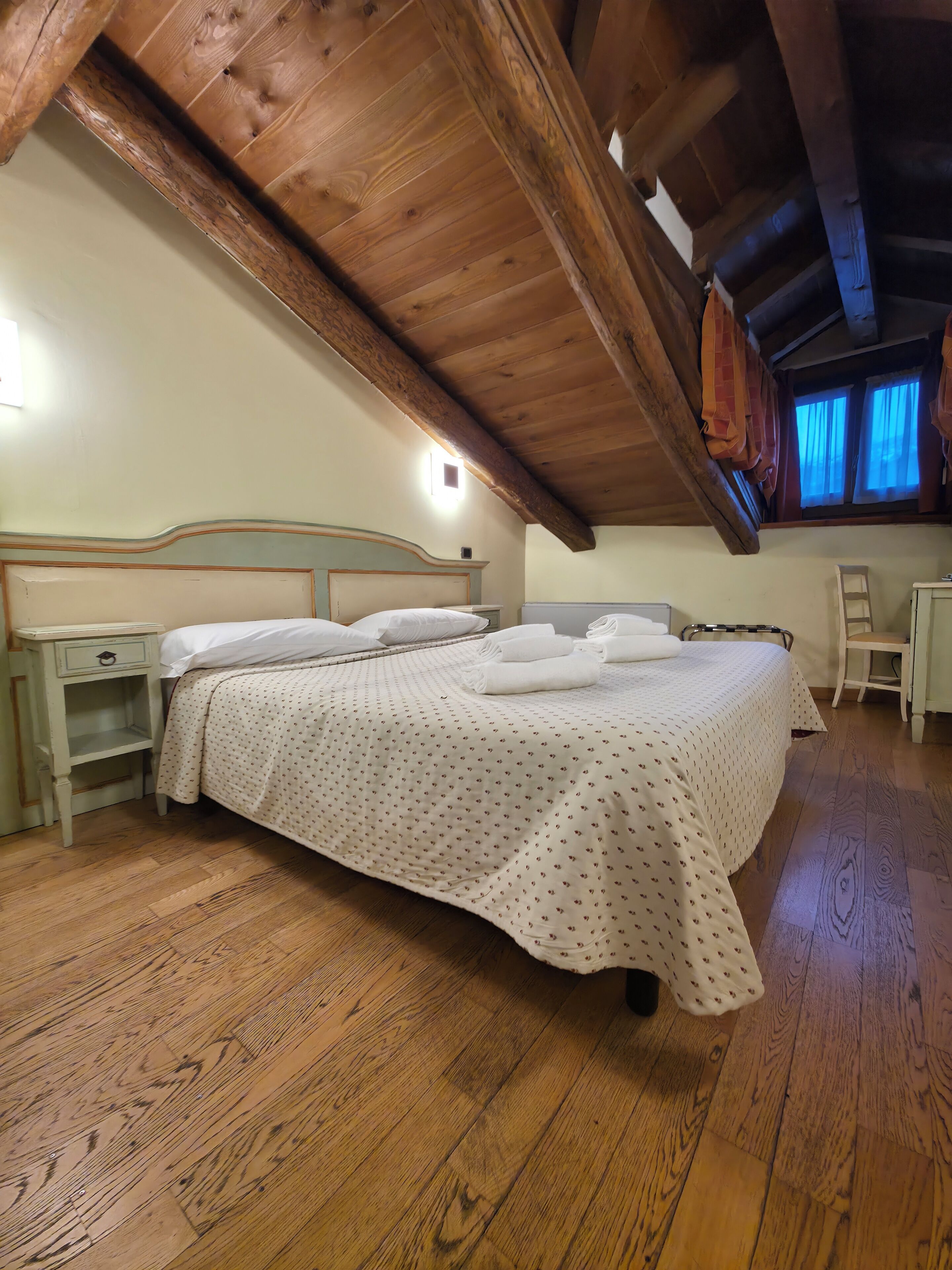 Un dormitorio con techo de madera, una cama con colcha blanca, una mesita de noche y un escritorio pequeño.