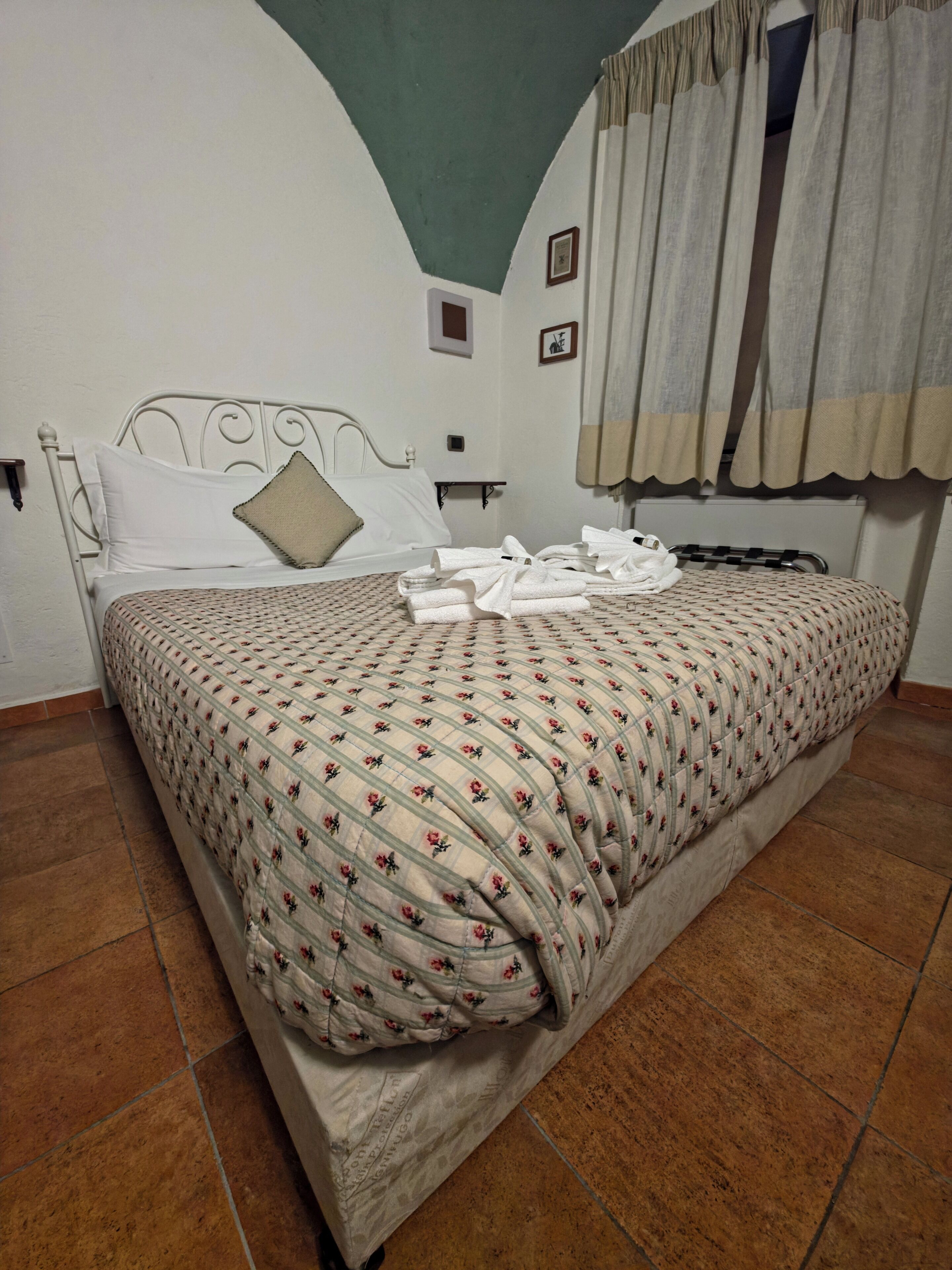 Una cama con una colcha estampada con motivos florales, un cabecero y un par de toallas sobre la cama.