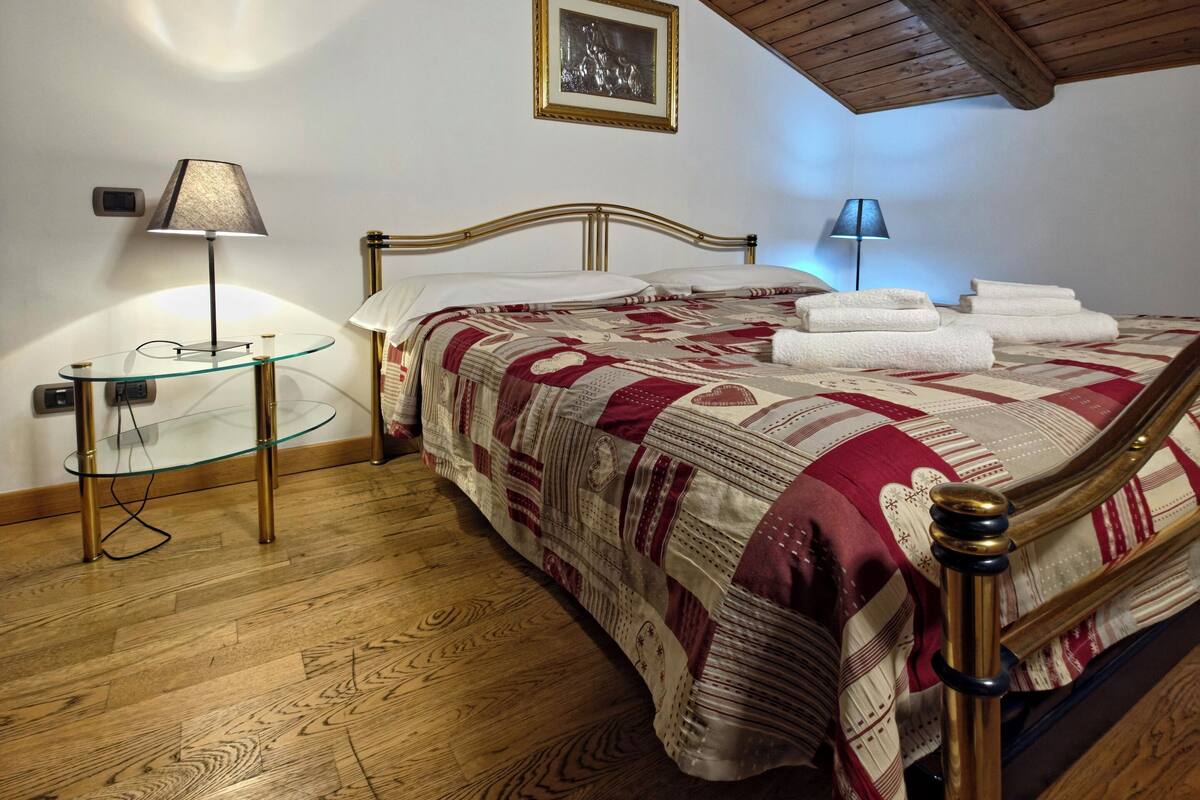 Ein Schlafzimmer mit Holzboden, einem Bett mit gemustertem Überwurf, einem Nachttisch mit Lampe und einem gerahmten Bild an der Wand.