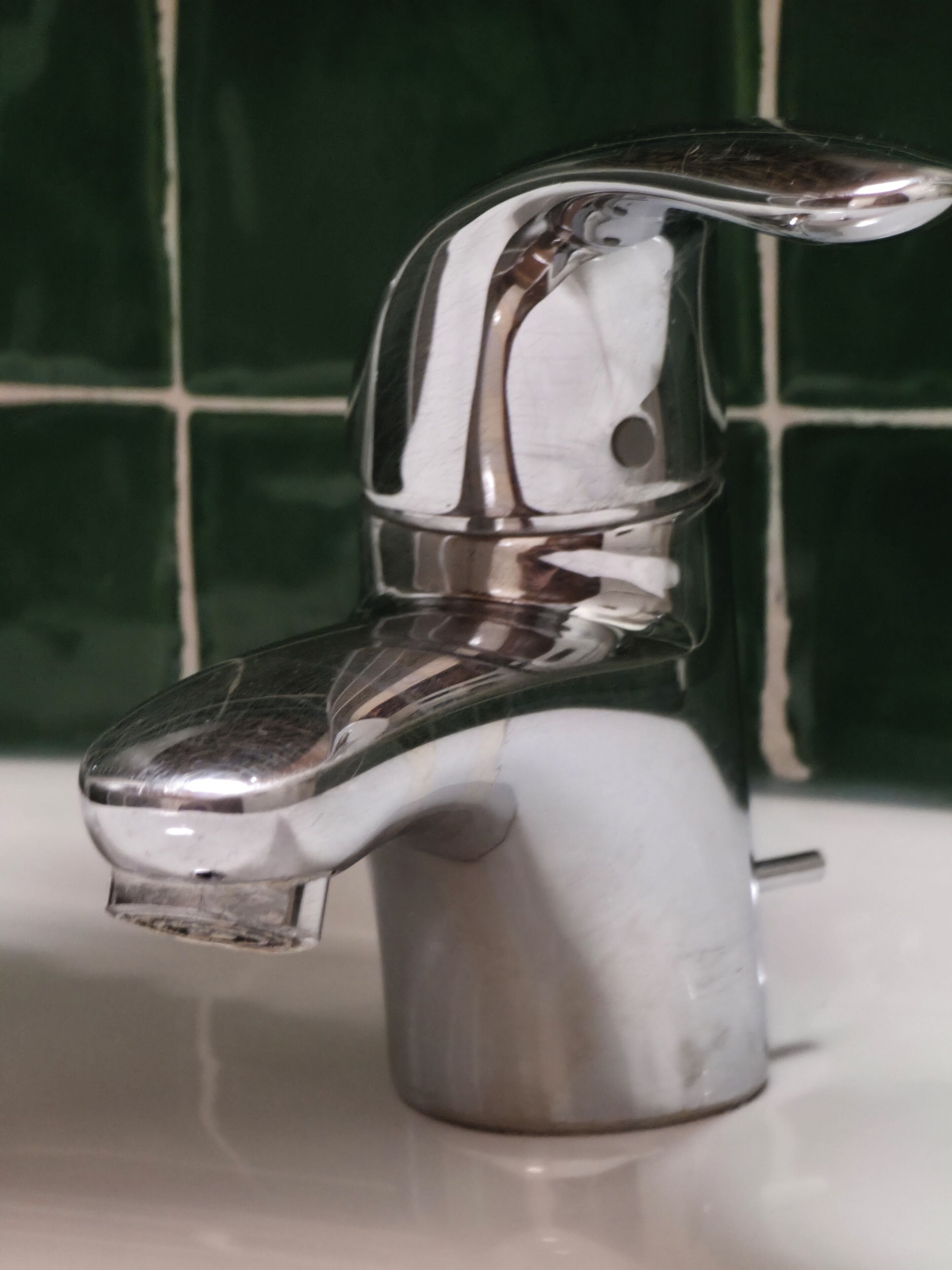 A chrome faucet with a single handle on a white sink.
