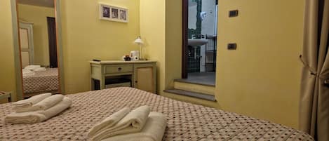 A hotel room with a bed, a desk, a mirror, a television, and a bathroom visible through an open door.