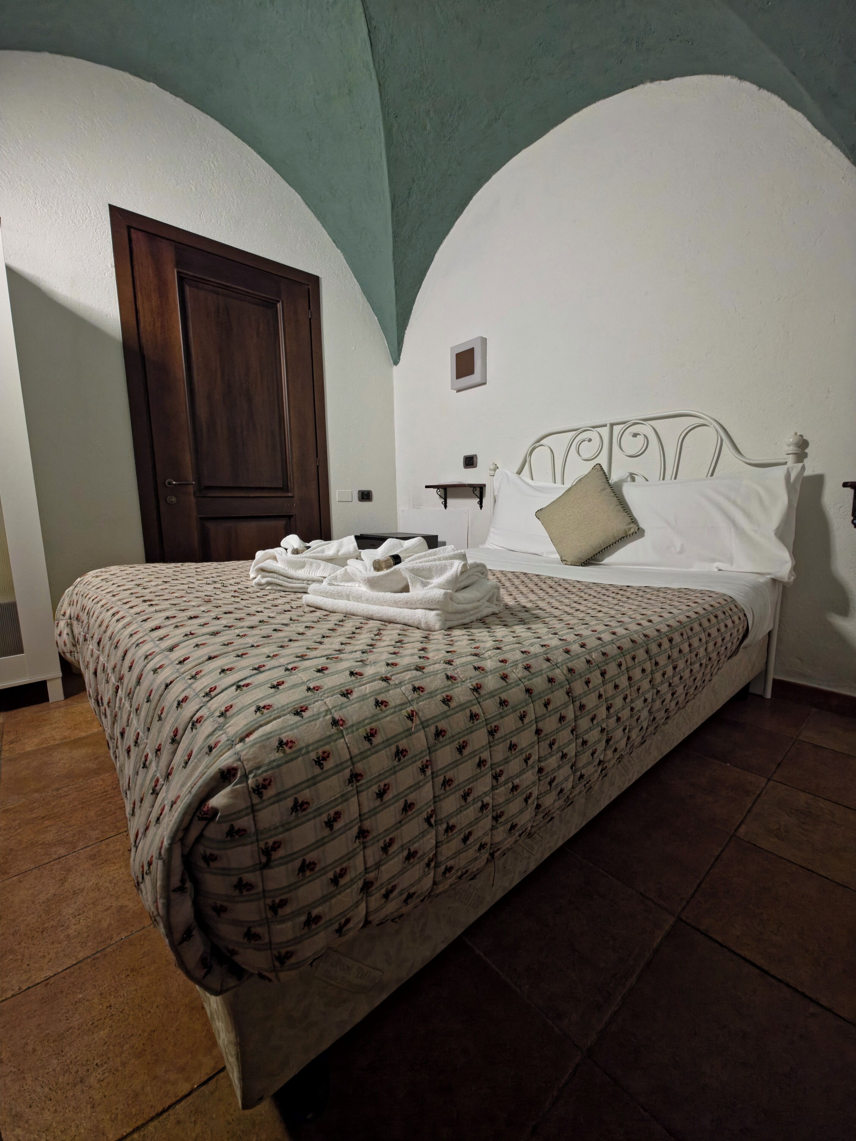 Un lit avec une couvre-lit à motifs floraux, une tête de lit blanche et une porte en bois en arrière-plan.