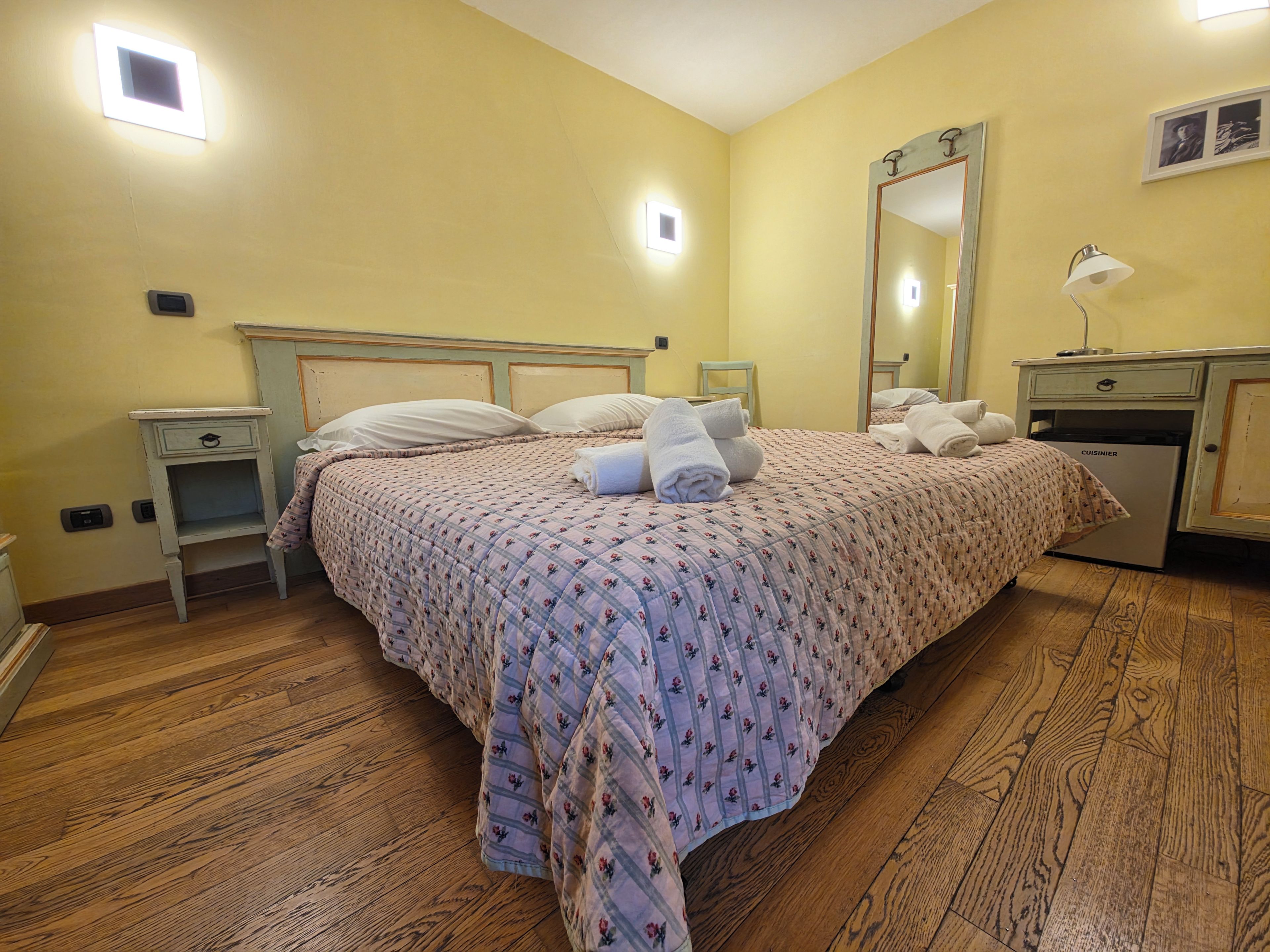Une chambre d’hôtel comprenant un lit, des tables de chevet, un miroir, une lampe et un mini-bar.
