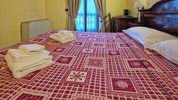 Habitación de hotel con techo de madera, una cama con colcha estampada, un televisor montado en la pared y un balcón visible a través de la ventana.