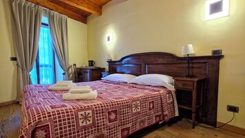 A bedroom with a wooden ceiling, a bed with a patterned bedspread, a bedside table with a lamp, and a nightstand with a kettle.