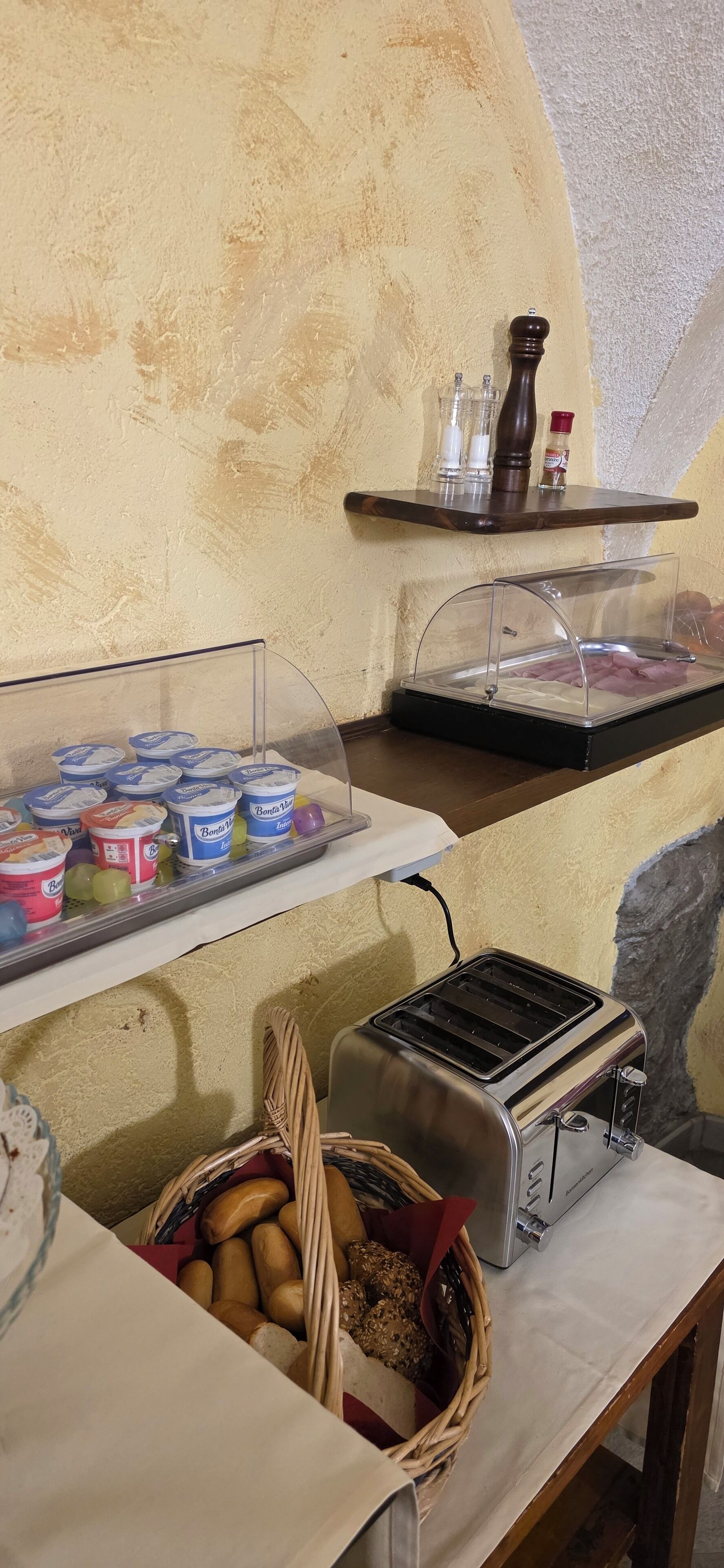 Un bufé de desayuno con recipientes de yogur, una tostadora y una cesta de pan.