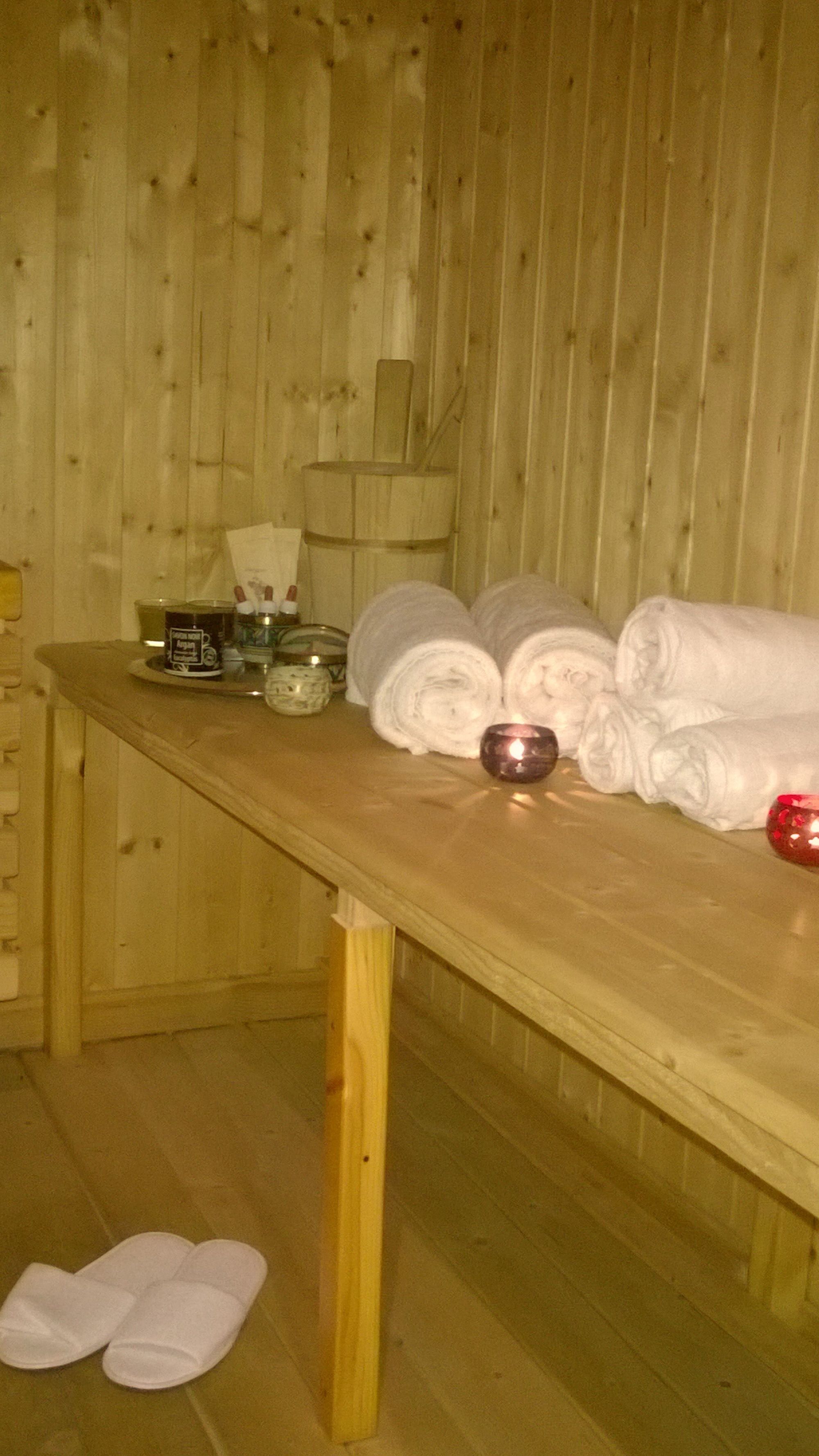 Eine Holzbank mit Handtüchern, einer Kerze und Pflegeprodukten in einem Raum mit Holzwänden.