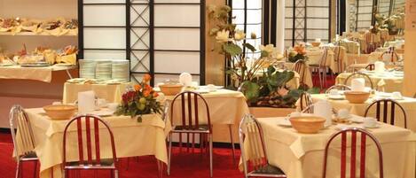 Un salón de banquetes con mesas dispuestas para un evento formal, destacando centros de mesa florales y manteles blancos.