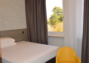 Habitación de hotel con cama, ventana con cortinas, una silla y pared con diseño de mapa.
