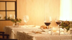 A dining table set with wine glasses, a vase with flowers, and a plate of food.