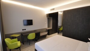 A modern hotel room with a bed, a desk, two chairs, a television, and a wardrobe.