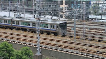 A train on multiple tracks with overhead electrical lines, surrounded by buildings and trees.