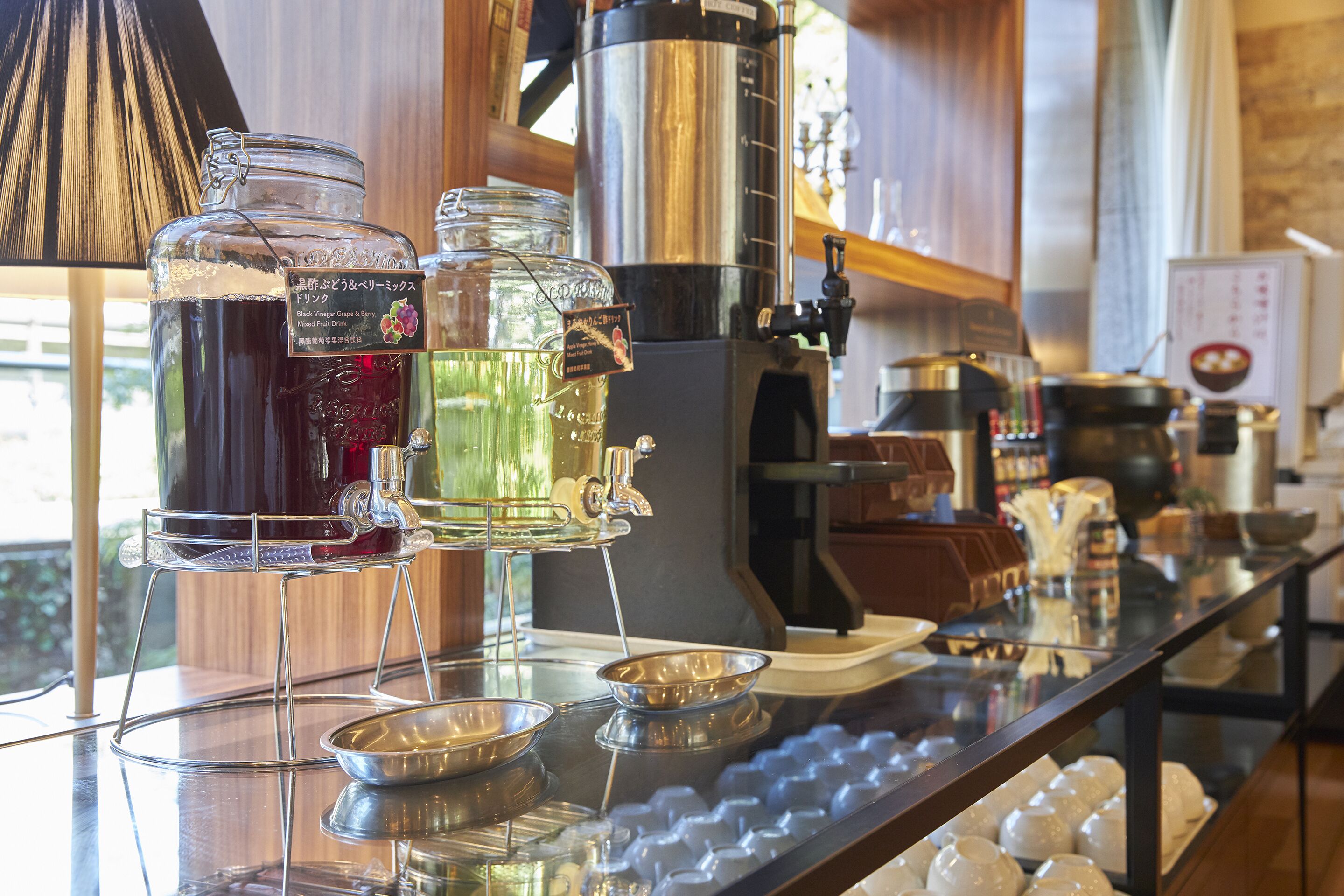 A bar area with a coffee machine, various drink dispensers, and a selection of glasses on a glass counter.