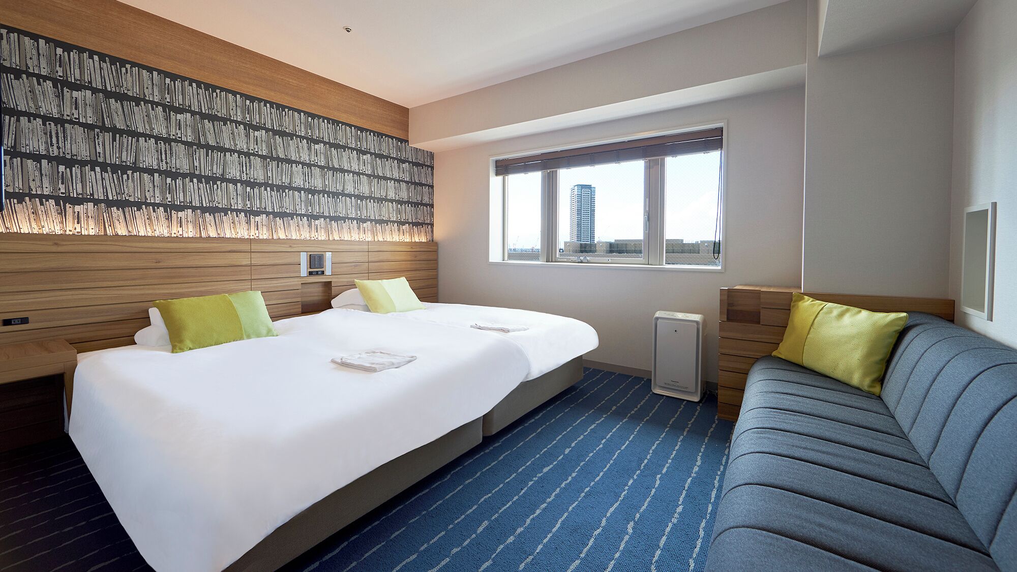 A hotel room with a large bed, a sofa, a wall-mounted heater, and a window with a city view.