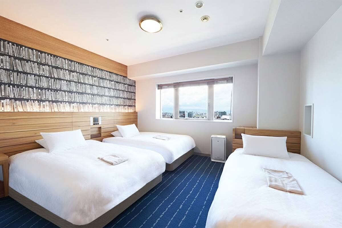 A hotel room with two beds, a large window, and a wall with a patterned design.