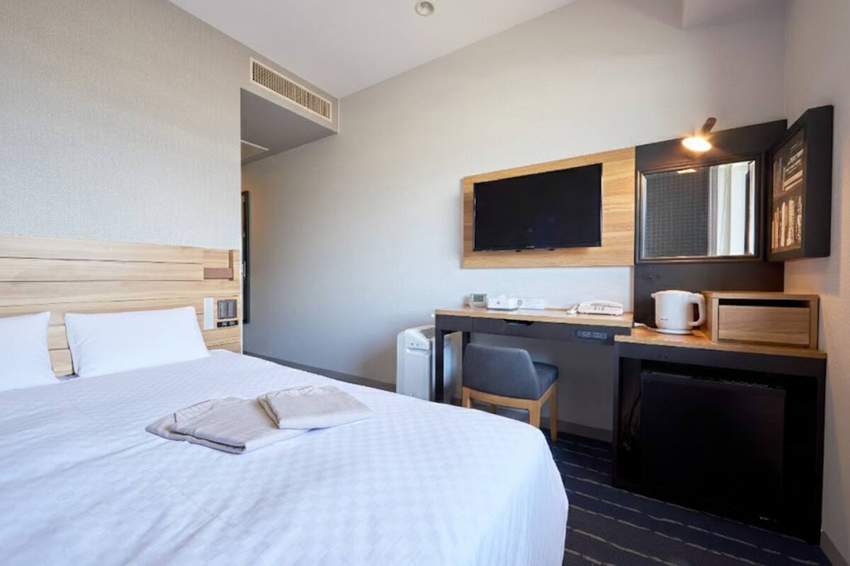 A hotel room with a bed, a desk, a chair, a coffee maker, and a television.