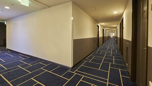 Un largo pasillo de hotel, estrecho, con alfombra estampada, puertas a ambos lados e iluminación empotrada en el techo.