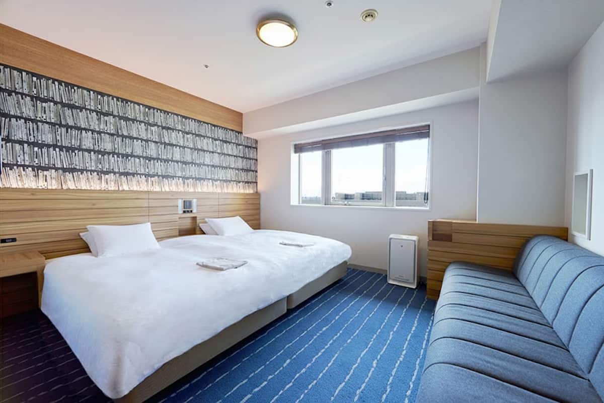 A hotel room with a large bed, a sofa, a window, and a wall-mounted artwork.