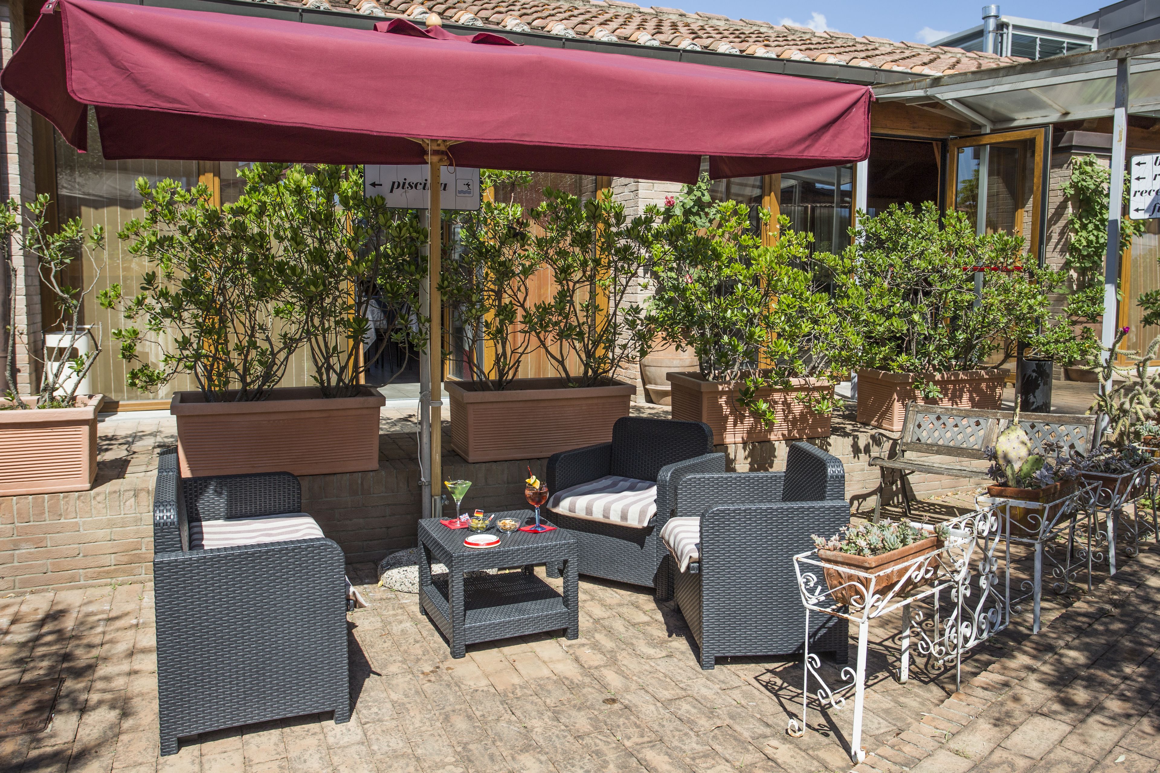 Un patio al aire libre con muebles de mimbre, un paraguas rojo y plantas en macetas.
