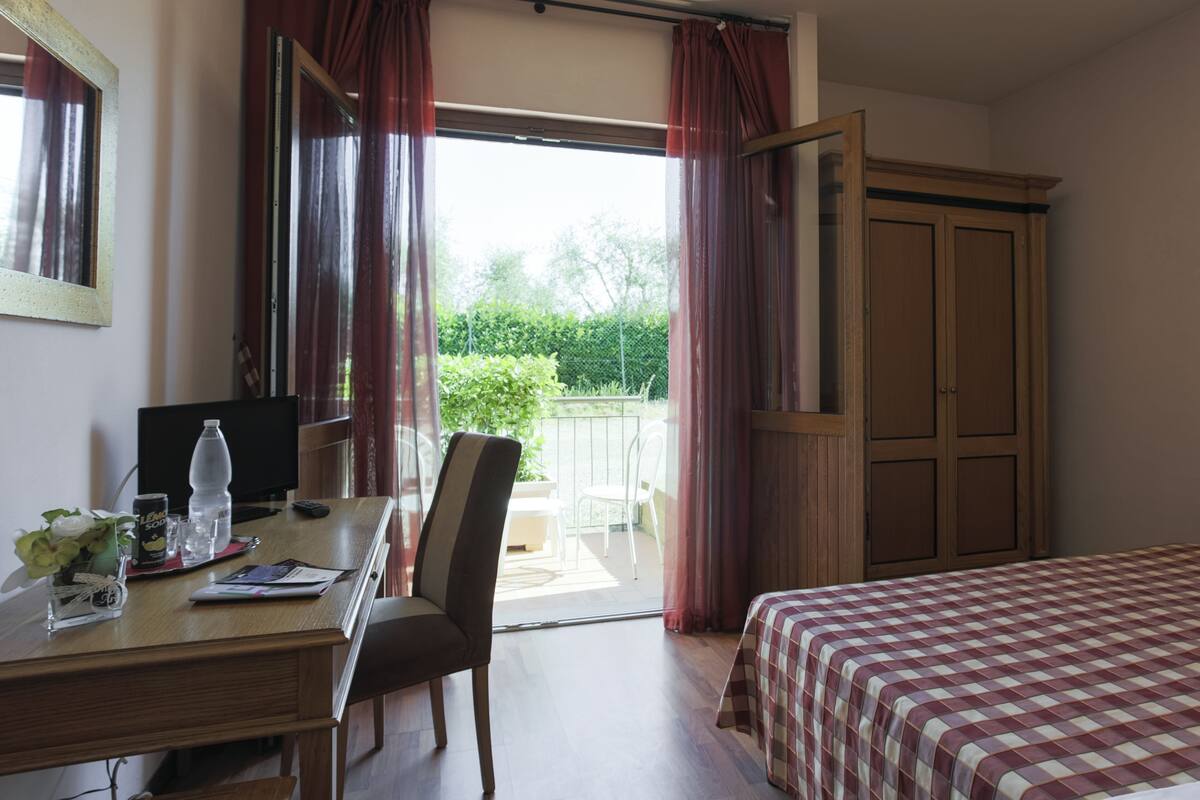 Een kamer met een bed, een bureau met stoel, een televisie en een raam met gordijnen.