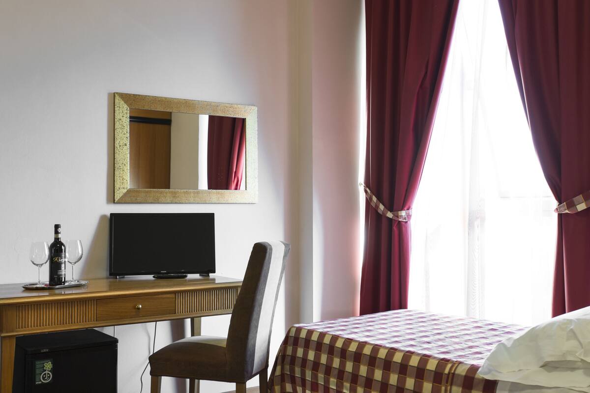 Een hotelkamer met een bed, een bureau met een computer, een stoel, een televisie en een minibar.