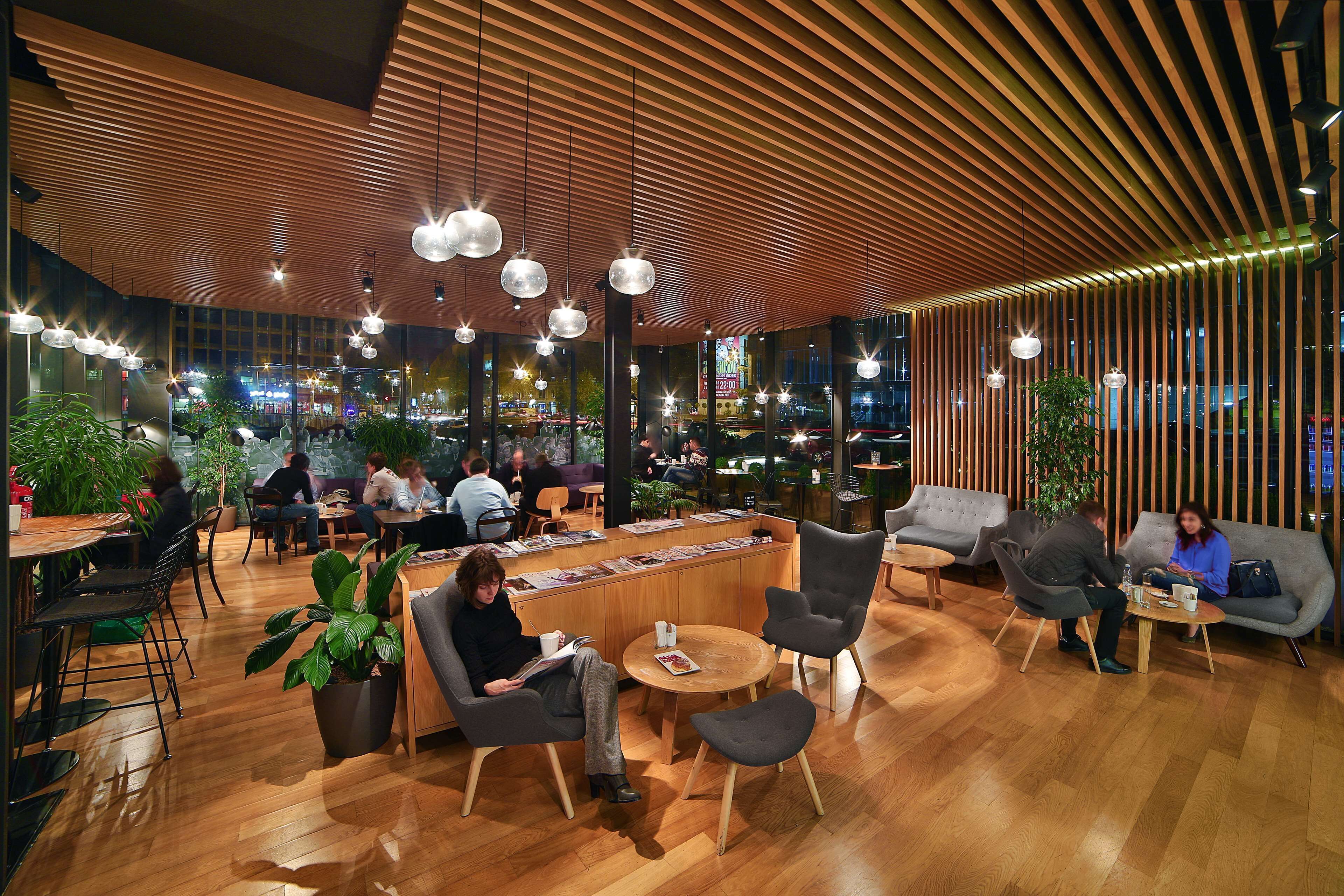 A modern indoor space with wooden slatted ceilings, round tables, and comfortable seating areas.
