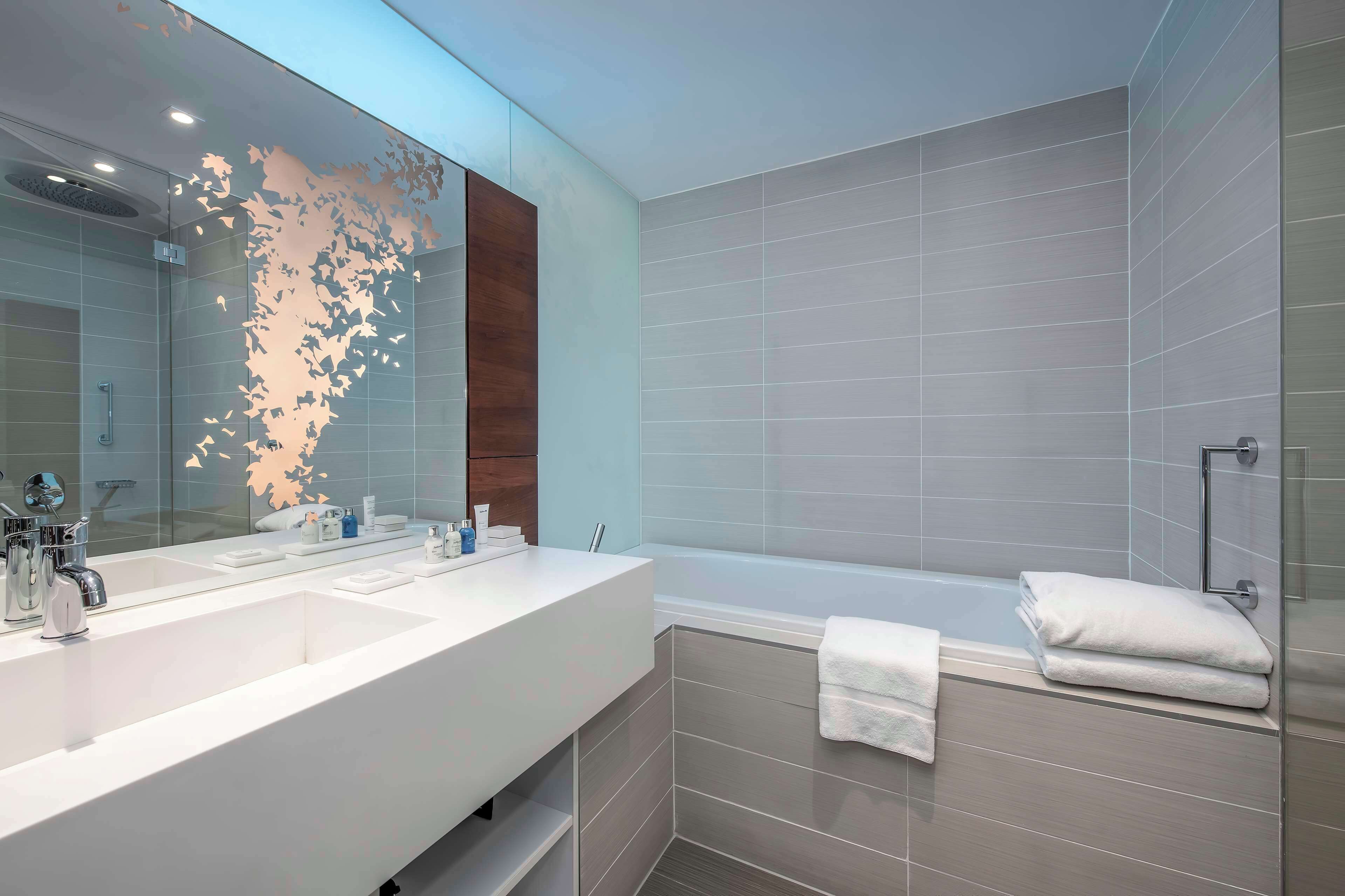 A modern bathroom with a large mirror, two sinks, a bathtub, and a shower.