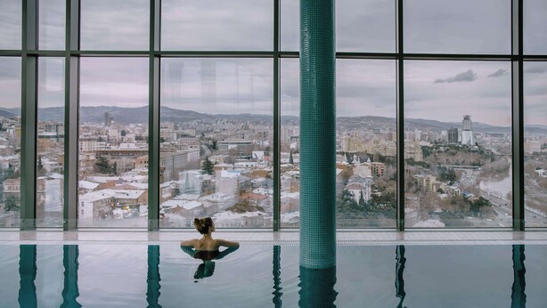 Une grande piscine intérieure avec de larges baies vitrées donnant sur le paysage urbain.