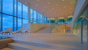 Un vaste espace intérieur doté d’un escalier menant à un niveau supérieur, de grandes fenêtres et d’un espace piscine avec des chaises longues.