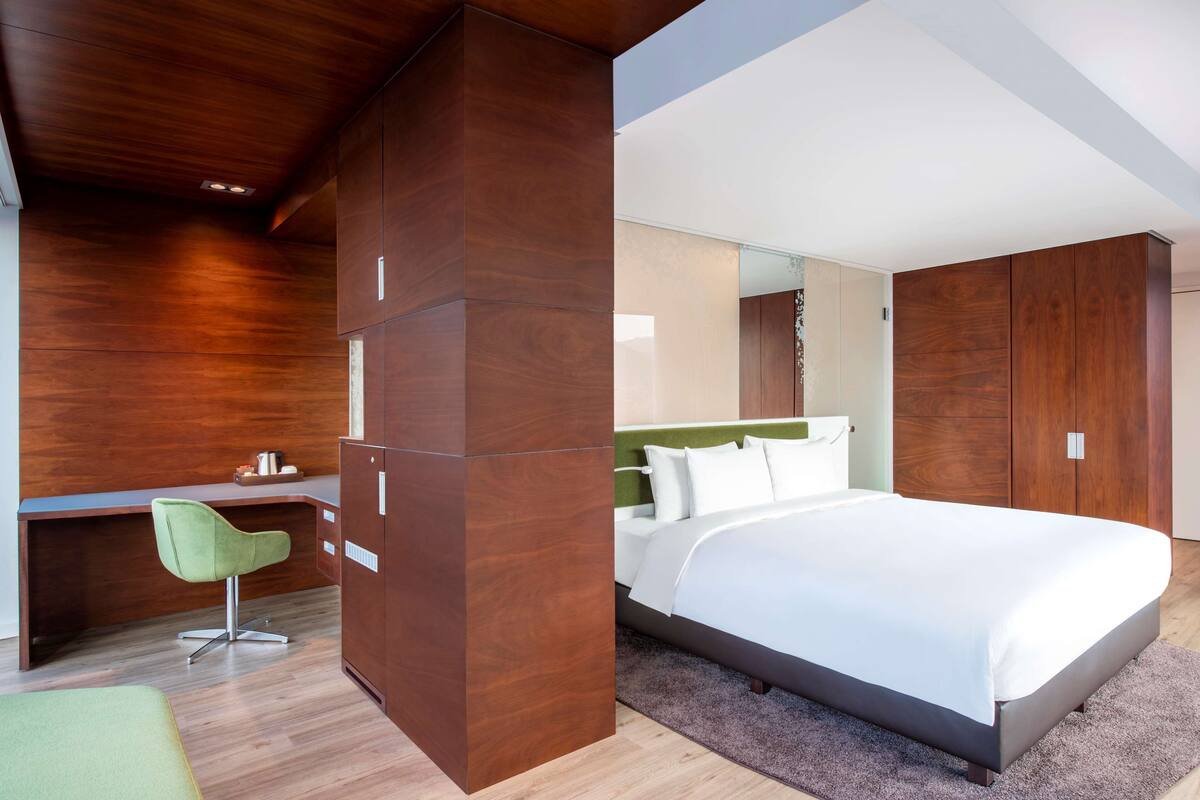 A modern bedroom with a large bed, a desk, and a green chair.