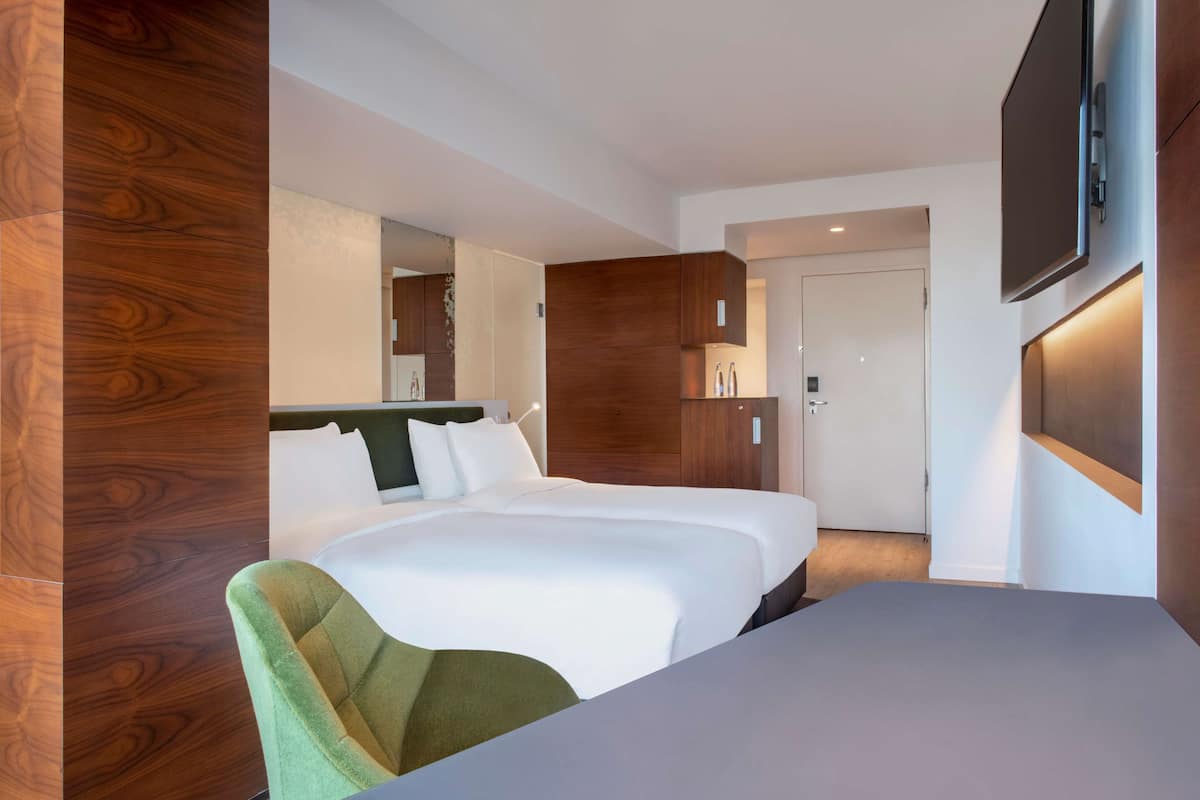 A hotel room with a large bed, a desk, a chair, and a TV mounted on the wall.