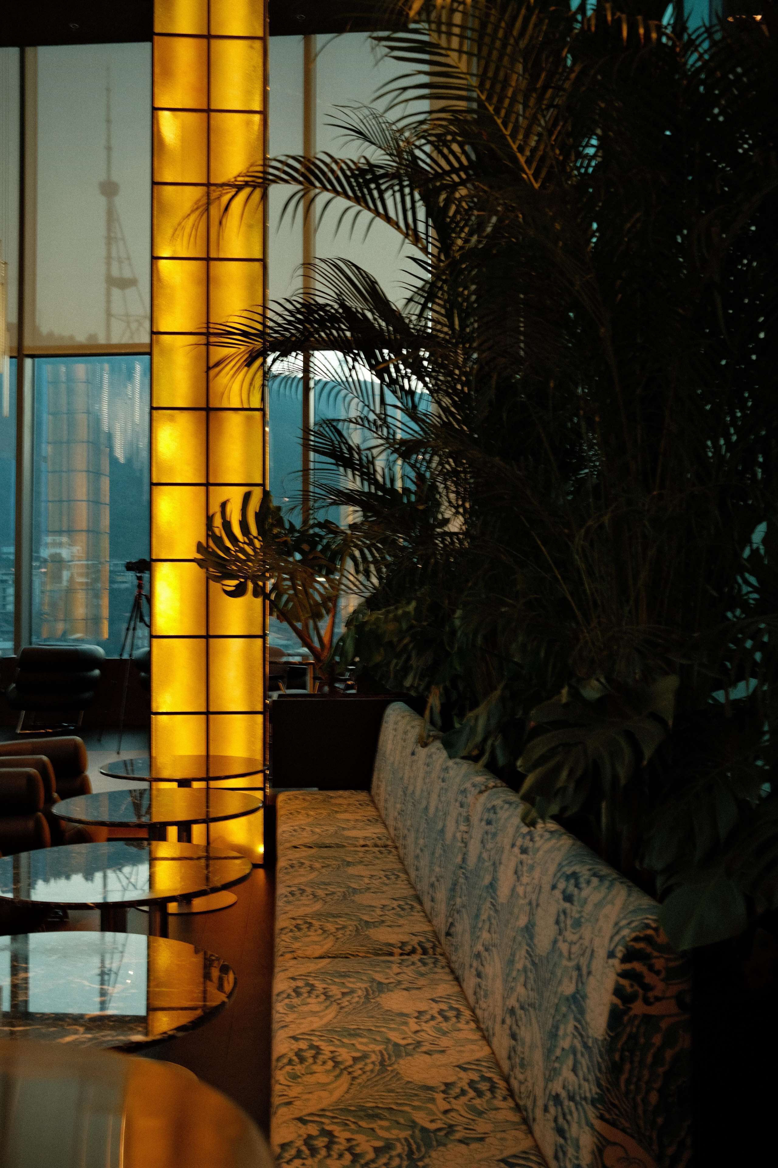 A modern interior with a large glass table, a sofa with a patterned upholstery, and a tall, illuminated column.