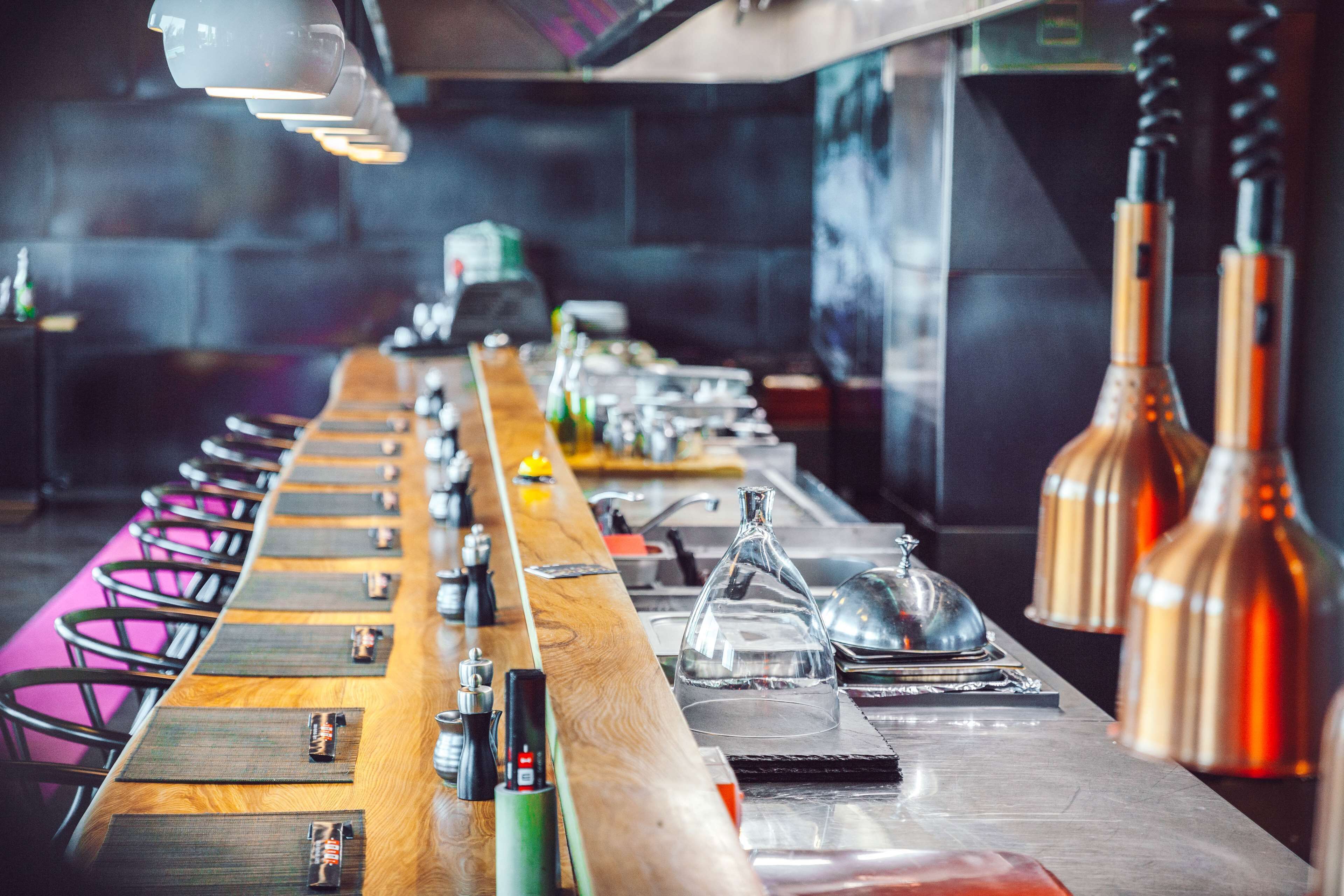 A long bar with a wooden counter, various bar tools, and copper-colored light fixtures.