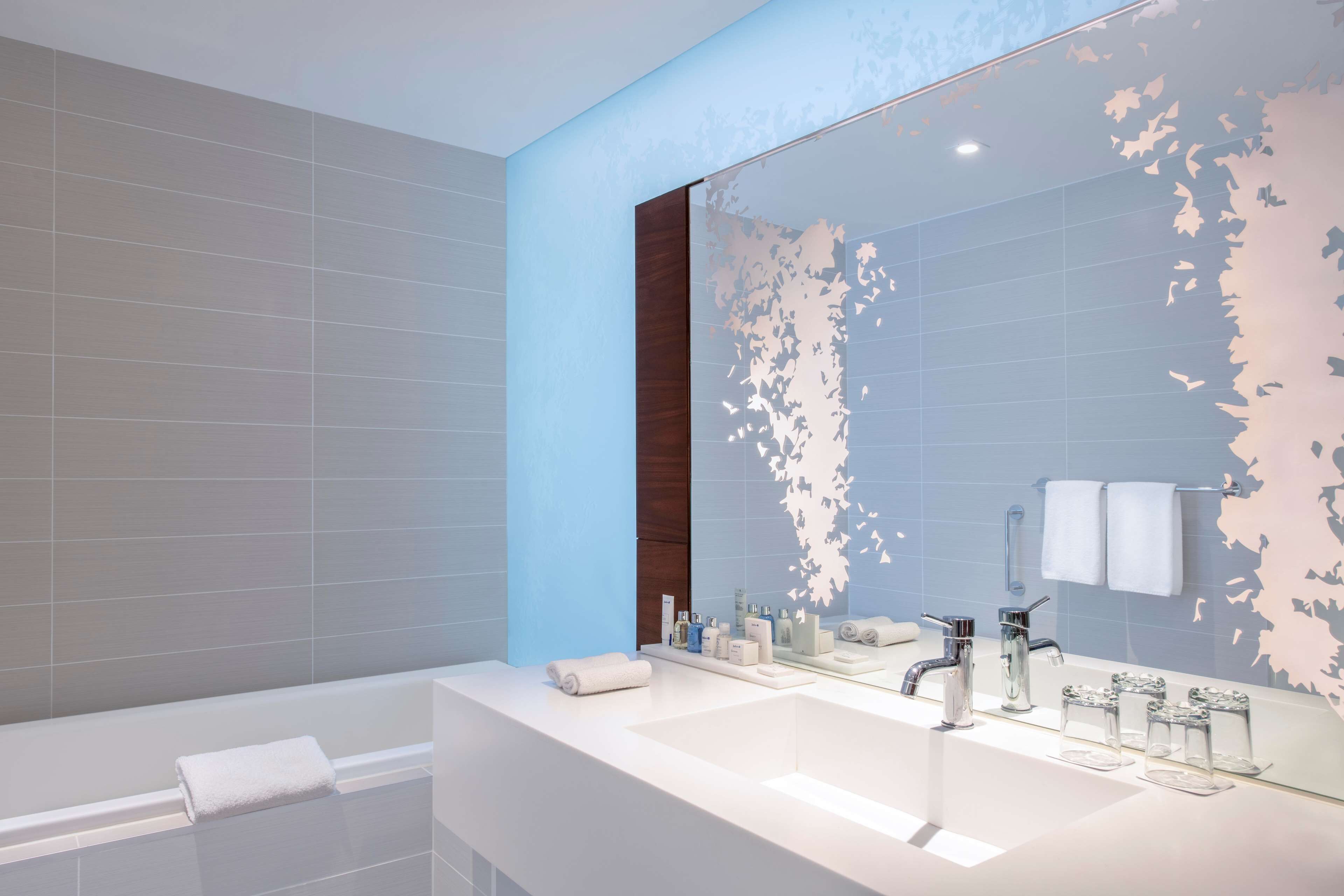 A modern bathroom with a large mirror, two sinks, a bathtub, and a towel rack.