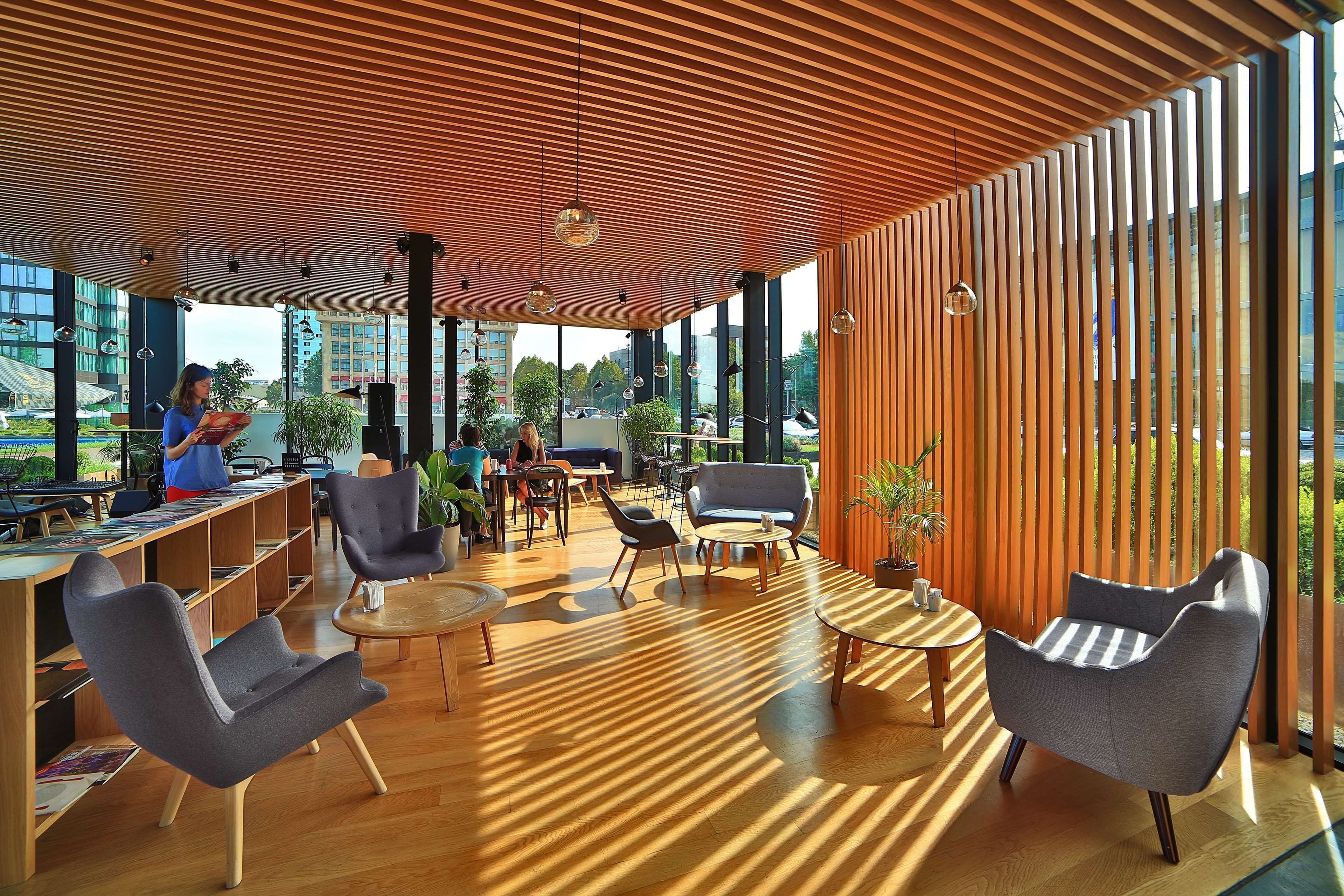 A modern indoor space with wooden slatted ceilings, large windows, and contemporary furniture.