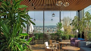 Un espace extérieur aménagé avec des tables et des chaises, entouré de plantes et offrant une vue sur le paysage urbain.