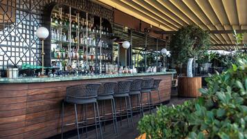 Un área de bar con mostrador de madera, varios taburetes y una amplia variedad de botellas y vasos.