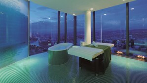 Une chambre d’hôtel située dans un immeuble de grande hauteur, offrant une vue sur la ville, équipée d’une baignoire et d’une table de massage.
