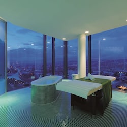 Enjoy a panoramic city view from the comfort of this stylish room, featuring a bathtub and massage table.